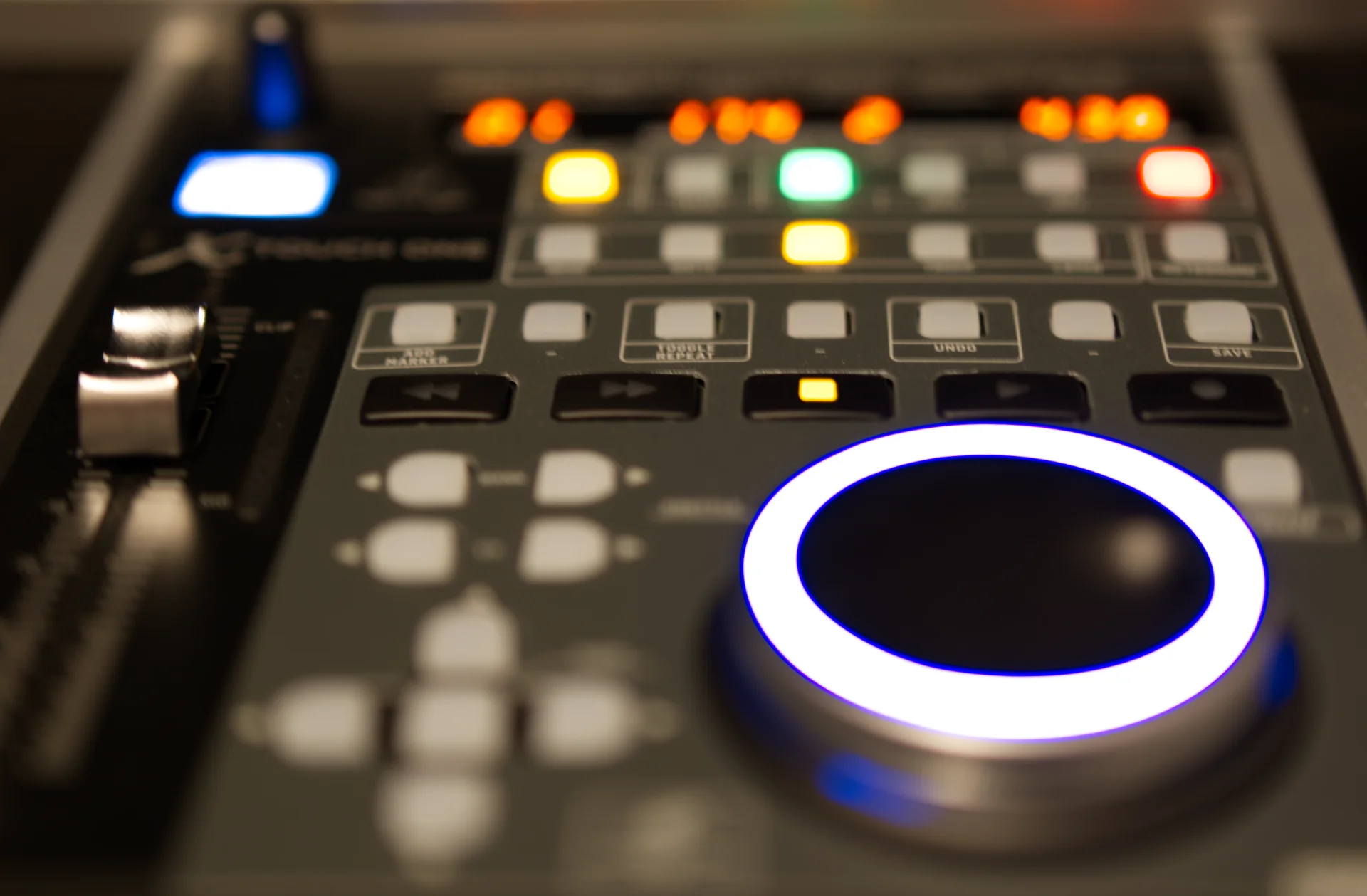 stylized photograph of a studio recording control surface, focused on a row of buttons (rewind, fast-forward, record, etc) with the rest of the panel moving out-of-focus